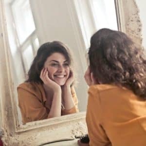 pexels-photo-774866-774866 A cheerful woman smiles at her reflection in a vintage-style mirror, exuding positivity and warmth.